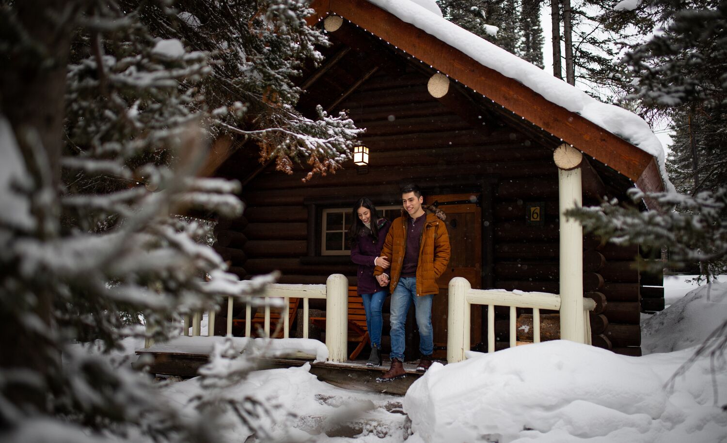 A couple walking out of a snowy cabin at Storm Mountain Lodge and Cabins in the winter in Banff National Park.